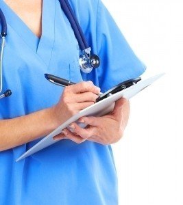 Healthcare professional in blue scrubs documenting patient information with a clipboard and pen.