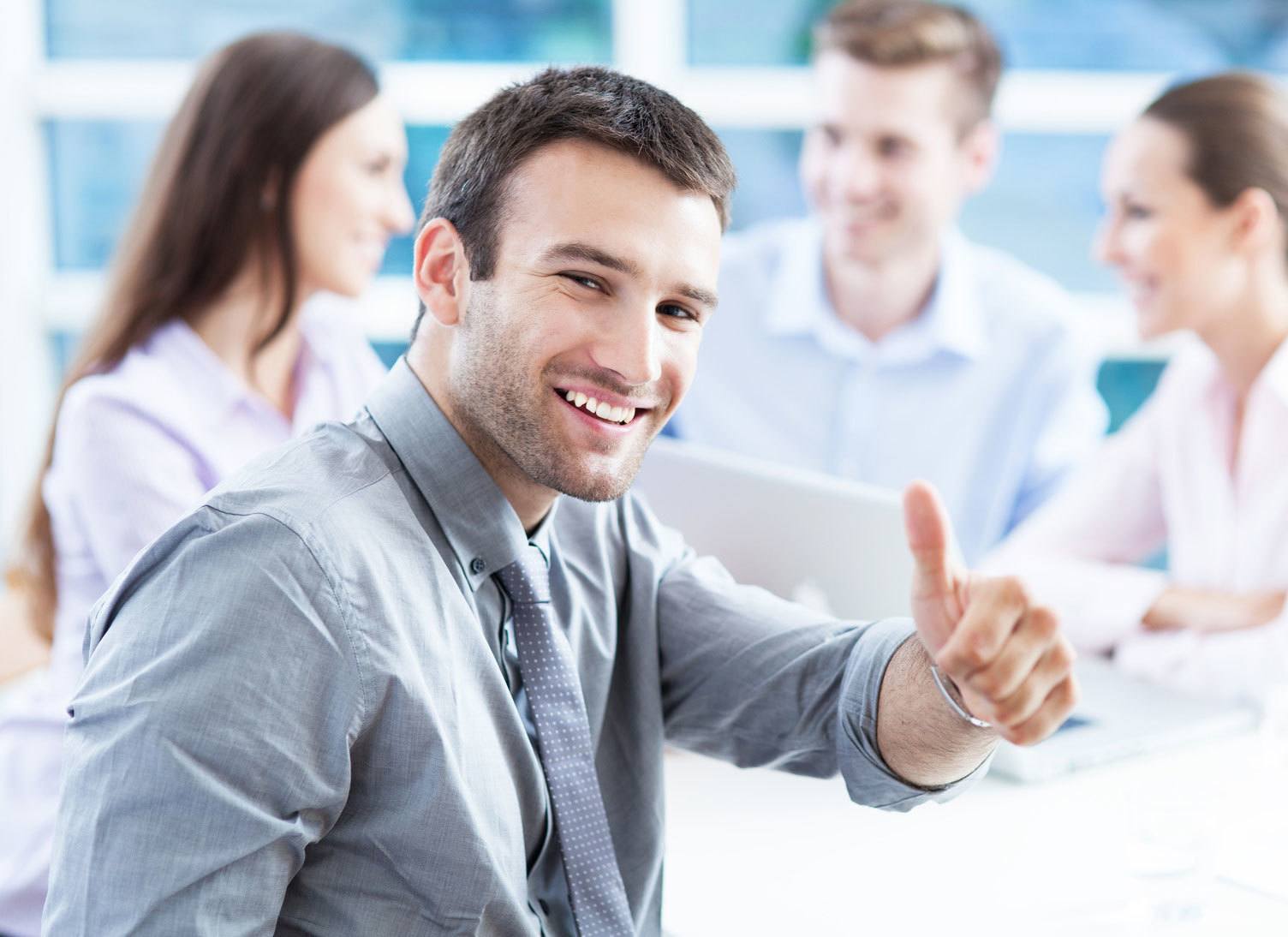 confident young man in a modern office celebrates teamwork with a thumbs up.