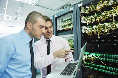 professionals collaborating in a server room, analyzing data on a laptop amidst server racks.