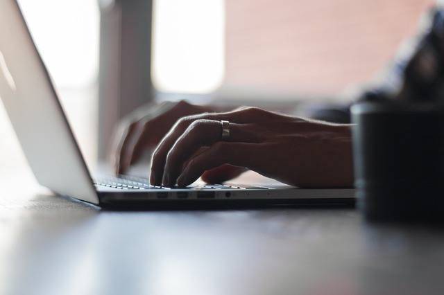 focused hands typing on a laptop in a warm, cozy workspace.