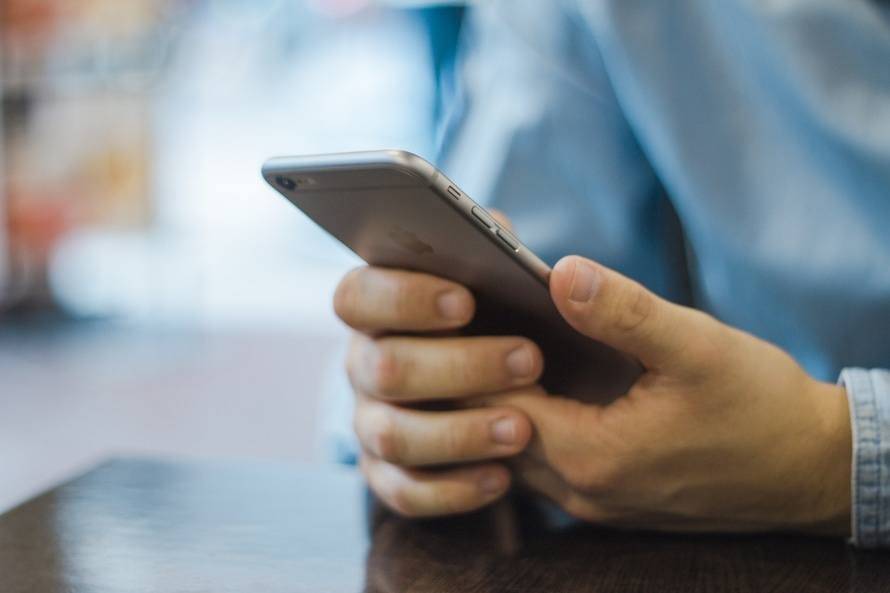 person in a light blue shirt engages with a smartphone in a cozy café setting.