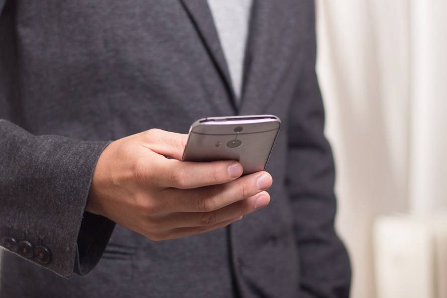 Professional in grey suit using smartphone in modern office setting.