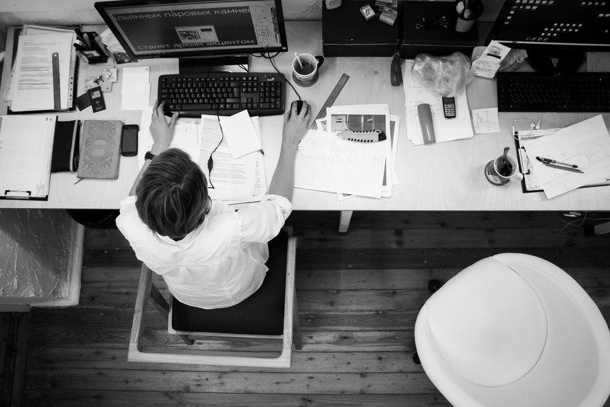 focused professional in a busy workspace with dual monitors and cluttered desk activities.