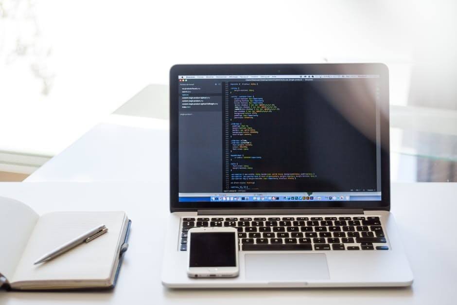 modern developer workspace with laptop, smartphone, and notebook, illuminated by natural light.