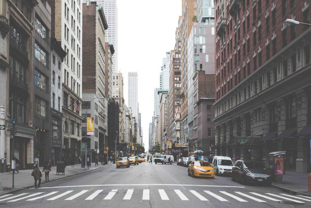 Lively city street scene with pedestrians and yellow taxis amid classic and modern architecture.