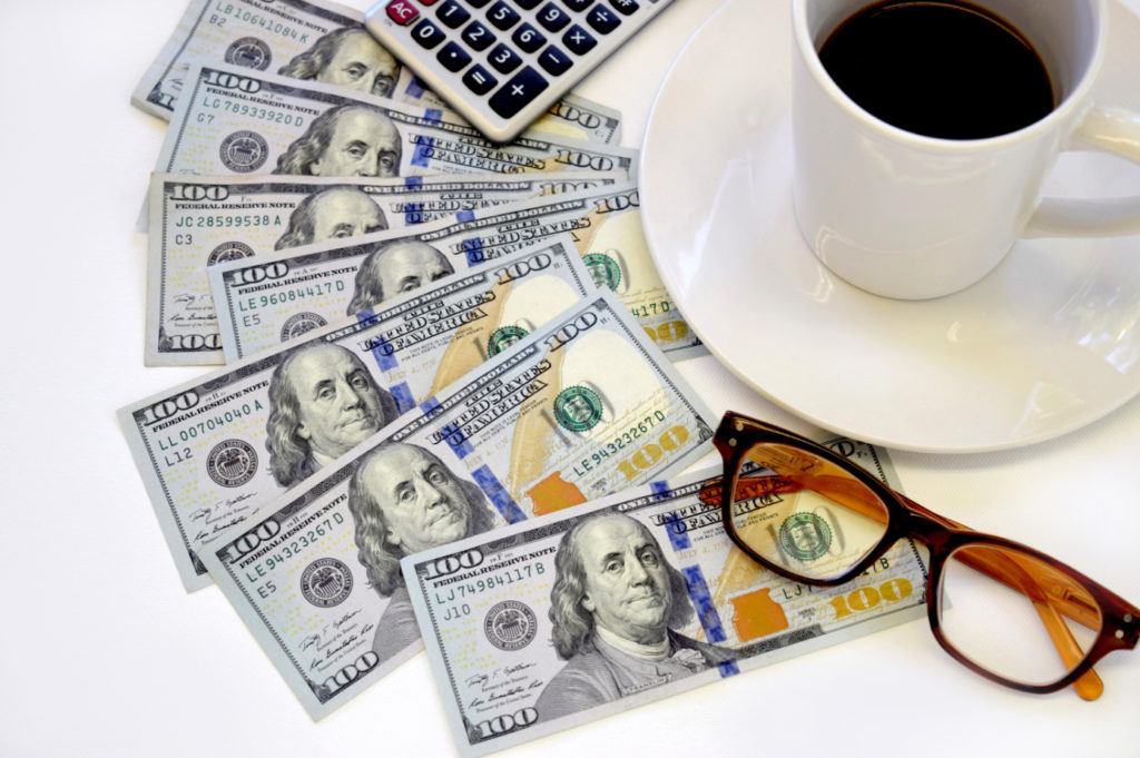 Finances and comfort: hundred-dollar bills, calculator, coffee, and eyeglasses for effective planning.