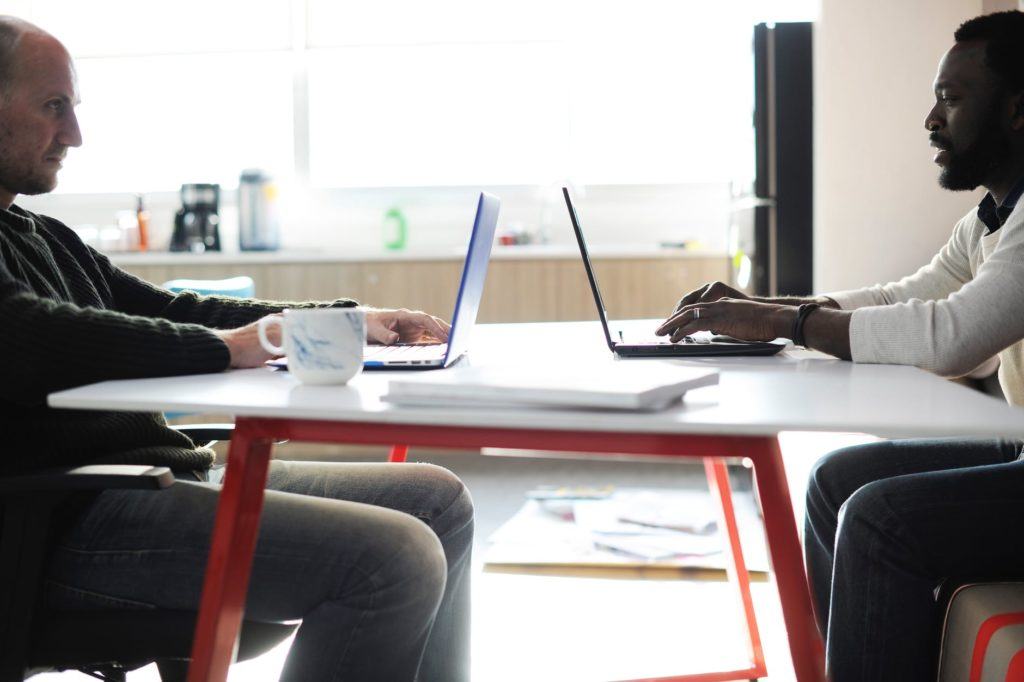 two professionals collaborating at a modern desk, focused on their laptops in a bright workspace.