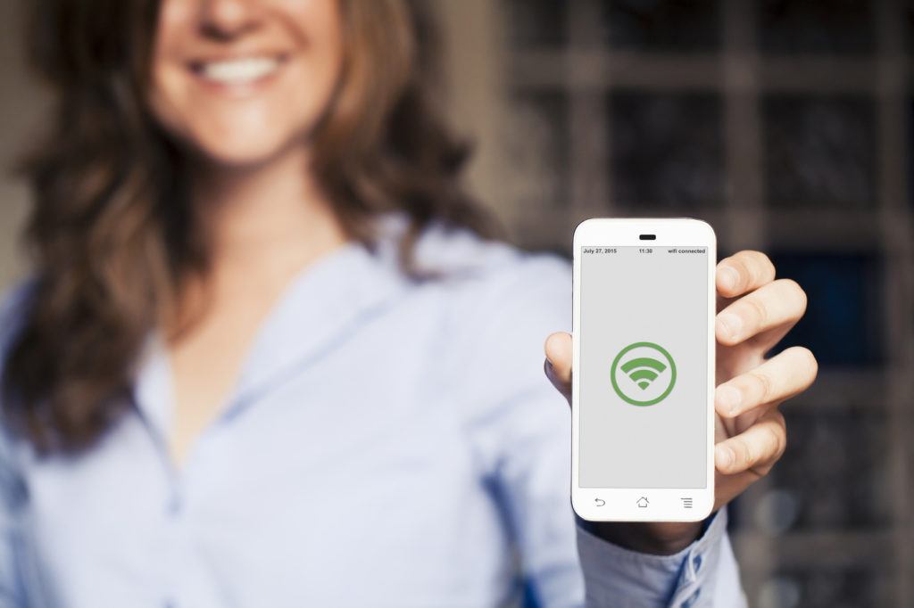 woman joyfully showcases smartphone with green wi-fi symbol in a modern, casual setting.