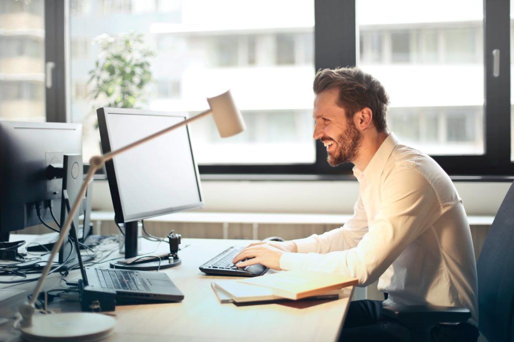 focused man in a white shirt working at a modern desk with multiple monitors.