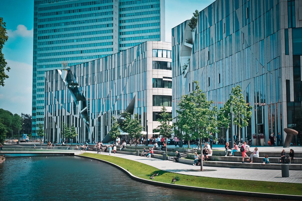 Modern urban landscape featuring sleek buildings and a tranquil waterway with people enjoying outdoor activities.