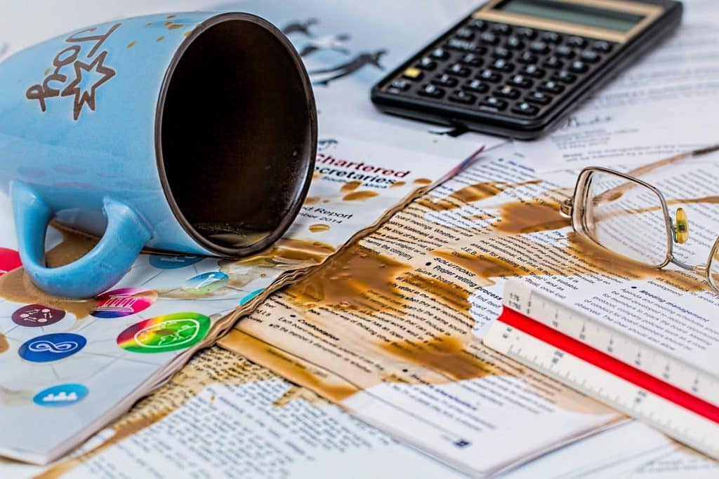 light blue mug spills coffee over papers in a chaotic study space filled with distractions.