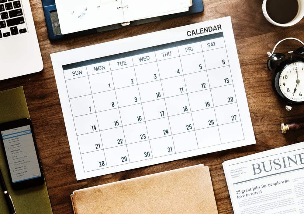 a desk with a calendar, cell phone, laptop and other office supplies