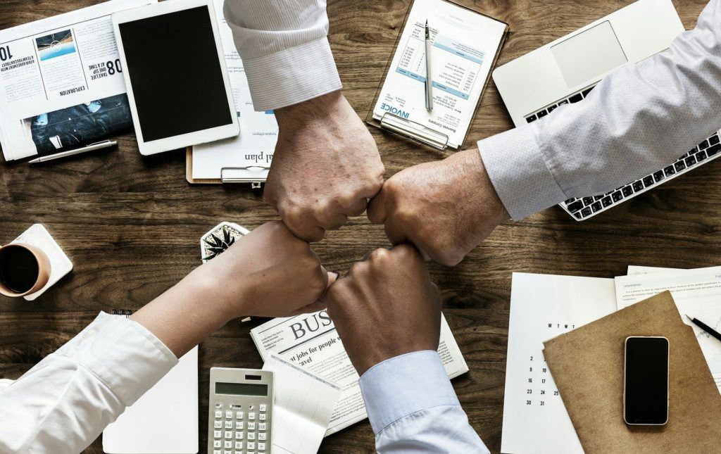 Diverse team celebrating collaboration with a fist bump in a bustling modern workspace.