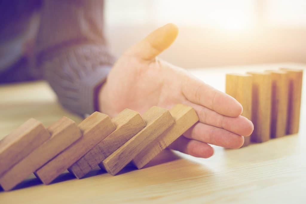 A hand stabilizes a precarious arrangement of wooden domino-like blocks on a warm table.