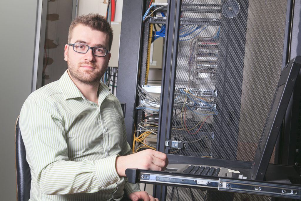 young it specialist working on laptop in a busy server room environment.