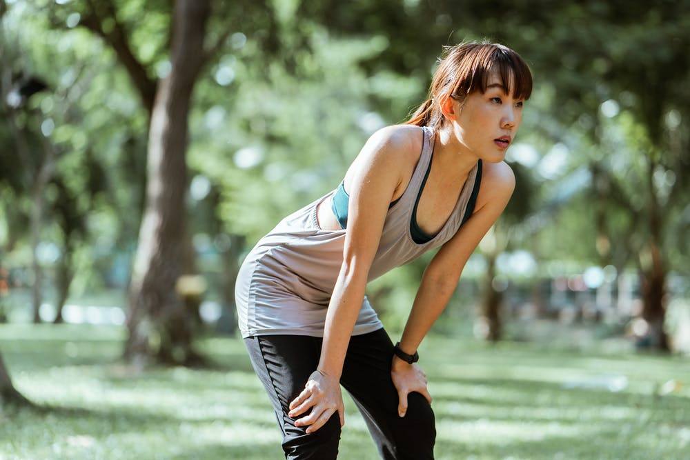 young woman resting after workout in a tranquil park, surrounded by lush greenery and sunlight.