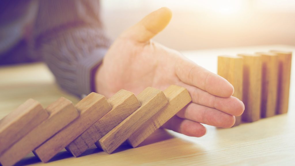 a hand poised over wooden dominoes symbolizes choices and their potential consequences on a table.