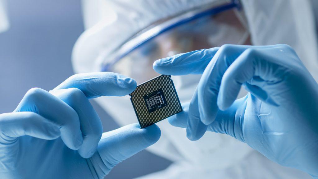 technician in protective suit carefully handles microprocessor in a cleanroom environment.