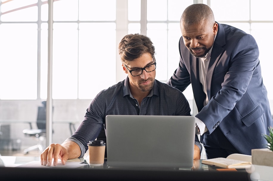 two professionals collaborate over a laptop in a bright, modern office setting.