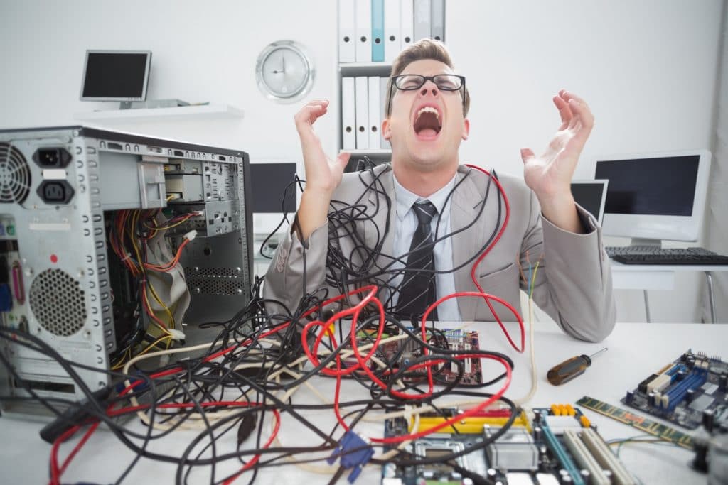 frustrated man in a suit struggles with tangled cables in a chaotic office setting.