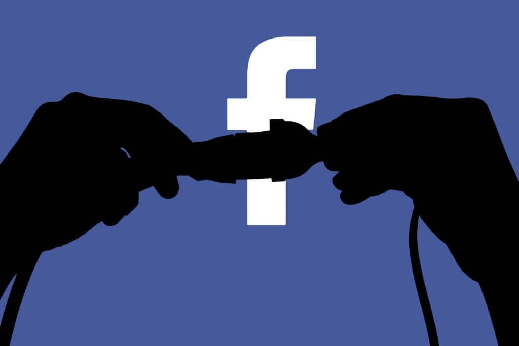 Silhouetted hands pulling apart a cord against the Facebook logo, symbolizing disconnection from social media.