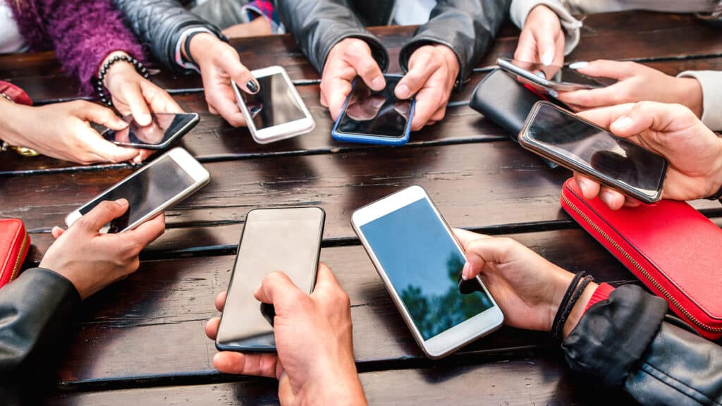 Diverse hands engage with smartphones, fostering connection in a cozy, rustic setting.