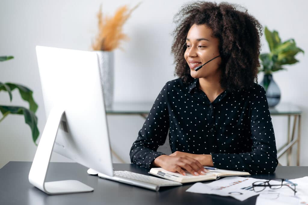 smiling woman engaged in a virtual meeting at a stylish, organized home office desk.