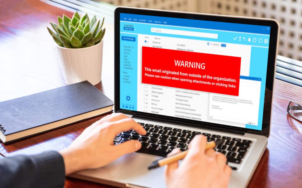 cybersecurity warning on laptop about risky email attachments and unrecognized sender in office.