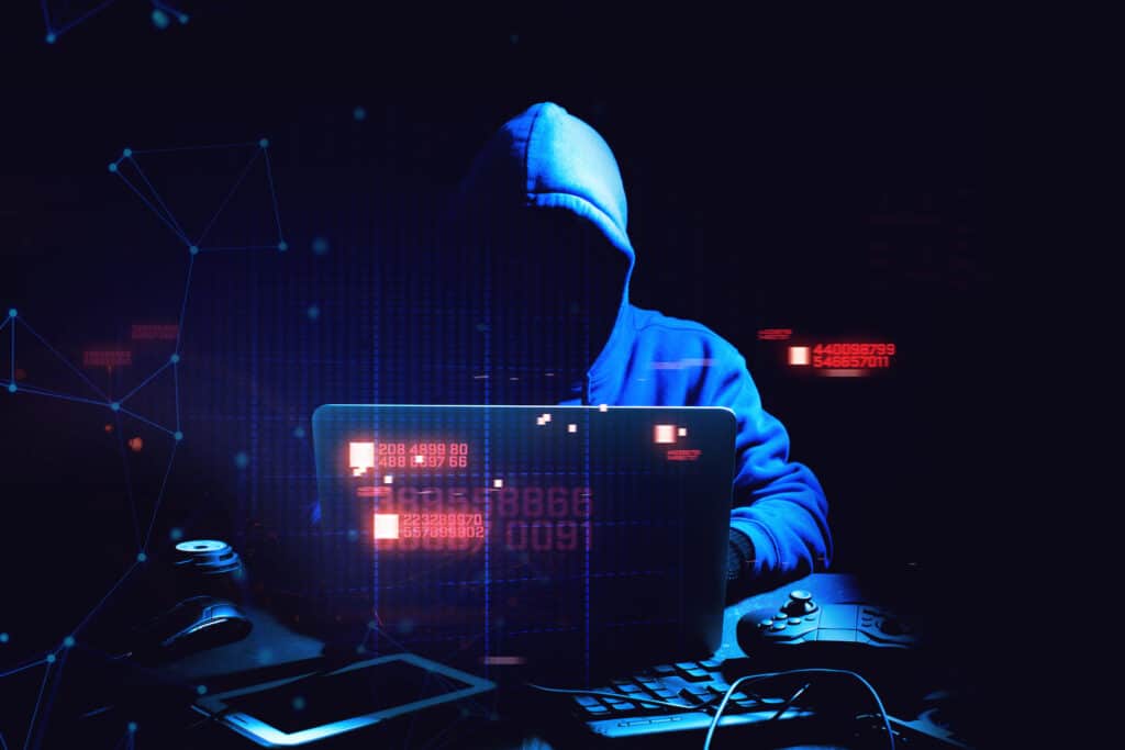 hooded figure hacking a laptop in the dark, symbolizing modern cybersecurity threats.